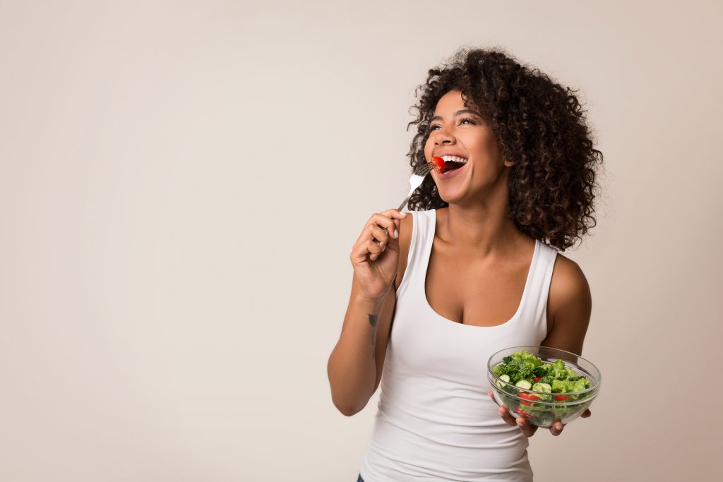 jeune femme souriante mangeant une salade saine sur fond clair.